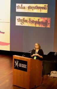 Anna Smol at podium giving a talk at Westmoot 2025. The slide behind her has the Old English words, "Eala earendel engla beorhtast" Photo by one of the professional photographers at Westmoot.